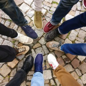 Image of legs of people standing in a circle and pointing their toes to each other. 