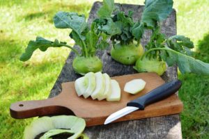 sliced and whole Kohlrabi sitting on a cutting board. There is a knife placed beside them. 