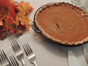 Pumpkin pie, forks, and a decorative gourd sitting on a Thanksgiving supper table