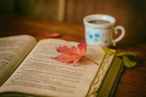 Open book on a table. The book is in Spanish, there is a cup of tea nearby, and there is a leaf lying in the middle of the book.