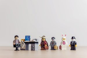 Lego people standing in a tidy queue while waiting to talk to someone who is sitting behind a desk. 