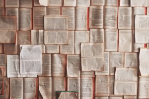 Opened books lying down on a flat surface. Every inch of the surface is covered in books. 