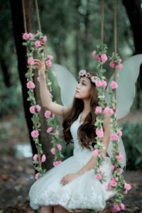 The personification of spring. She's sitting on a swing that's adorned with pink roses. 