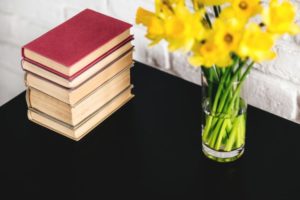 Stack of books sitting next to a vase of yellow flowers