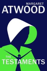The Testaments by Margaret Atwood book cover. Image on cover is of a handmaid wearing a green shawl and white cap. You can't see her face. 