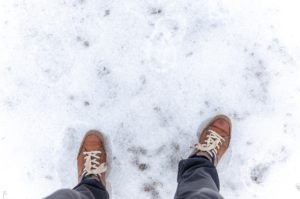 Image of a person's legs as they walk on a snowy, icy surface.