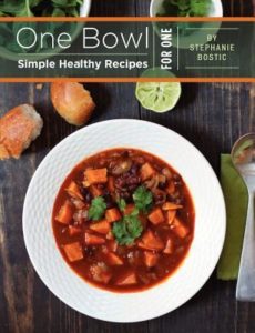 One Bowl: Simple Healthy Recipes for One by Stephanie Bostic. Book cover is of a bowl of hearty vegetable soup. There are two bread rolls, a lime, and a spoon sitting next to it. 