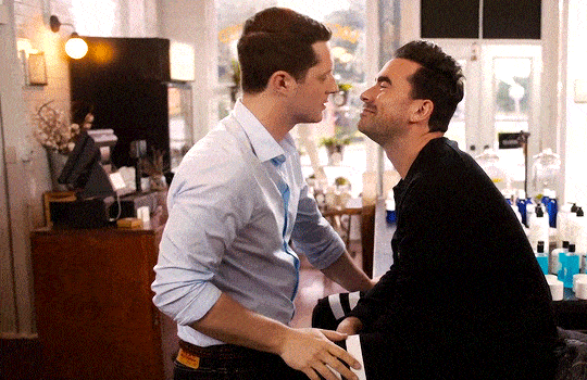 David and Patrick from Schitt's Creek standing in their store and kissing. 