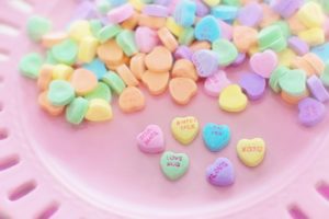 A pink plate covered in candy conversation hearts. The six hearts we can read say "soul mate," love bug," "sweet talk," "say yes," "love," and "xoxo."