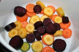 A bowl full of orange, yellow, green, and purple carrots sliced into round pieces. 