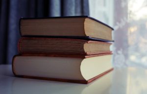 Three piled books on a white wooden table. 