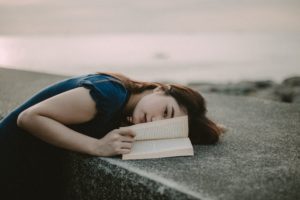 photo of woman lying down on a stone wall while holding the pages of a book open.