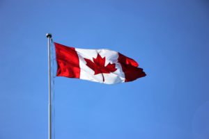 anadian flag on a flagpole blowing in the breeze. The sky behind the flag is bright blue and cloudless. 