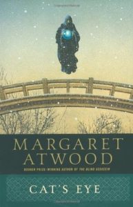 Cat's Eye  by Margaret Atwood book cover. Image on cover is of a hooded figure holding a glowing blue orb levitating above a bridge while snow falls on bare tree branches.