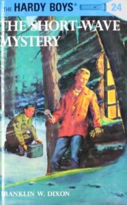 The Short-Wave Mystery (Hardy Boys, #24) by Franklin W. Dixon book cover. Image on cover is of one boy looking into a log cabin through its window while another boy crouches on the snow behind him. 