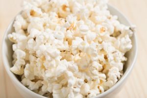 A white bowl filled with popcorn and sitting on a wooden table 