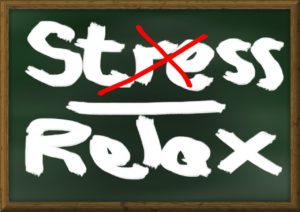 Chalkboard with the words stress and relax written on it. The word stres is crossed out with a red x. 