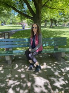 Woman sitting on a park bench underneath a large, shady tree. 