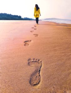 Woman walking barefoot on a beach as the tide comes in. Her footprints are straight and even across the sand.