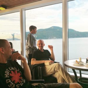 Two men and one preteen boy on the deck of a cruise ship smiling and talking. 