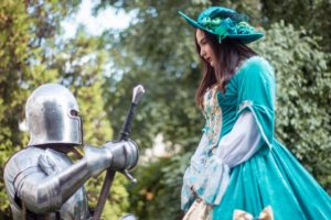 A knight kneeling in front of a woman who is wearing a medieval dress.