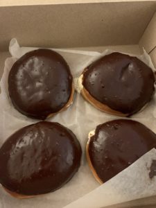 A cardboard box filled with four dairy-free boston creme donuts.