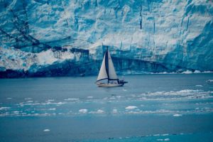A small sailboat sailing next to a large glacier. 