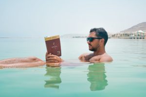 Man floating in a body of water while reading and wearing a pair of sunglasses