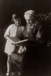 Senior woman sitting on chair while reading a book to a young girl 