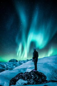 Person standing on snowy mountain while looking at aurora borealis at night 