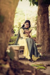 Woman reading book while sitting on a stone bench in a forest 