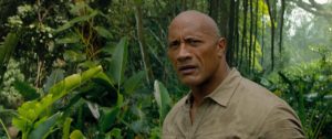 Dwayne Johnson as Dr. Xavier Smolder Bravestone. He's standing in a jungle. 