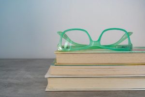 Green framed eyeglasses on top of a stack of three books