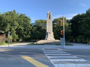 Lanscape photo of a forest, World War I monument, and a crosswalk. 