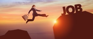 Woman leaping between boulders. The one she is leaping to has the word "job" on it. 