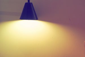 A blue lamp that is turned on and releasing light against a plain white wall. 