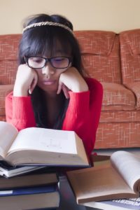 A girl with a bored expression on her face reading a book.