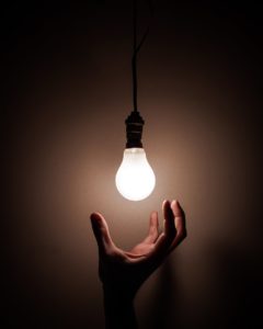 A hand reaching up to touch a bright lightbulb