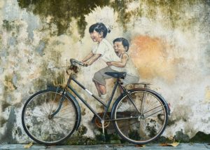 Bicycle leaning up against a mural of two children riding a bike so that it looks like they're riding a real bike