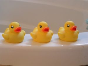 Three rubber duckies sitting on the edge of a white bathtub