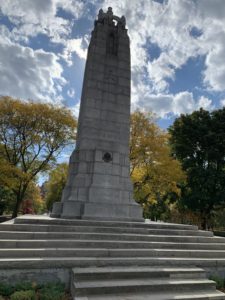 close-up shot of a World War I monument in a park whose trees have begun turning colours in October. 