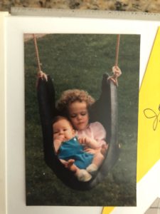 A young girl and her infant brother cuddling together in a tire swing
