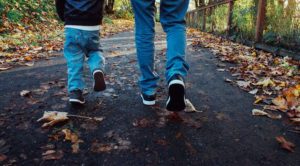 Parent and child taking a walk on an autumn-leaf-strewn path. 