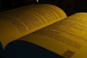 A close up photo of an opened book being illuminated by warm, yellow light.