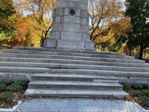 Close-up photo of World War I monument at a park. the monument is on a series of stone steps and surrounded by evergreen bushes. 