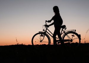 Silhoutte of person pushing an upright bicycle on a hill at dusk