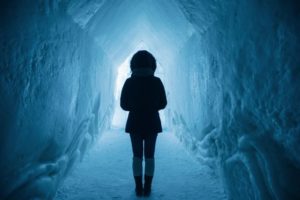 Person standing in a 6+ foot tall tunnel built into thick walls of snow and ice. 