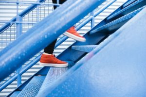 Photo of person's legs and orange shoes as they climb a flight of blue stairs. 