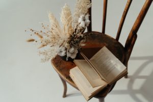 a book and a dried bundle of flowers sitting on a wooden chair 