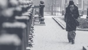 black and white photo of person walking alone on a city sidewalk during a snowstorm